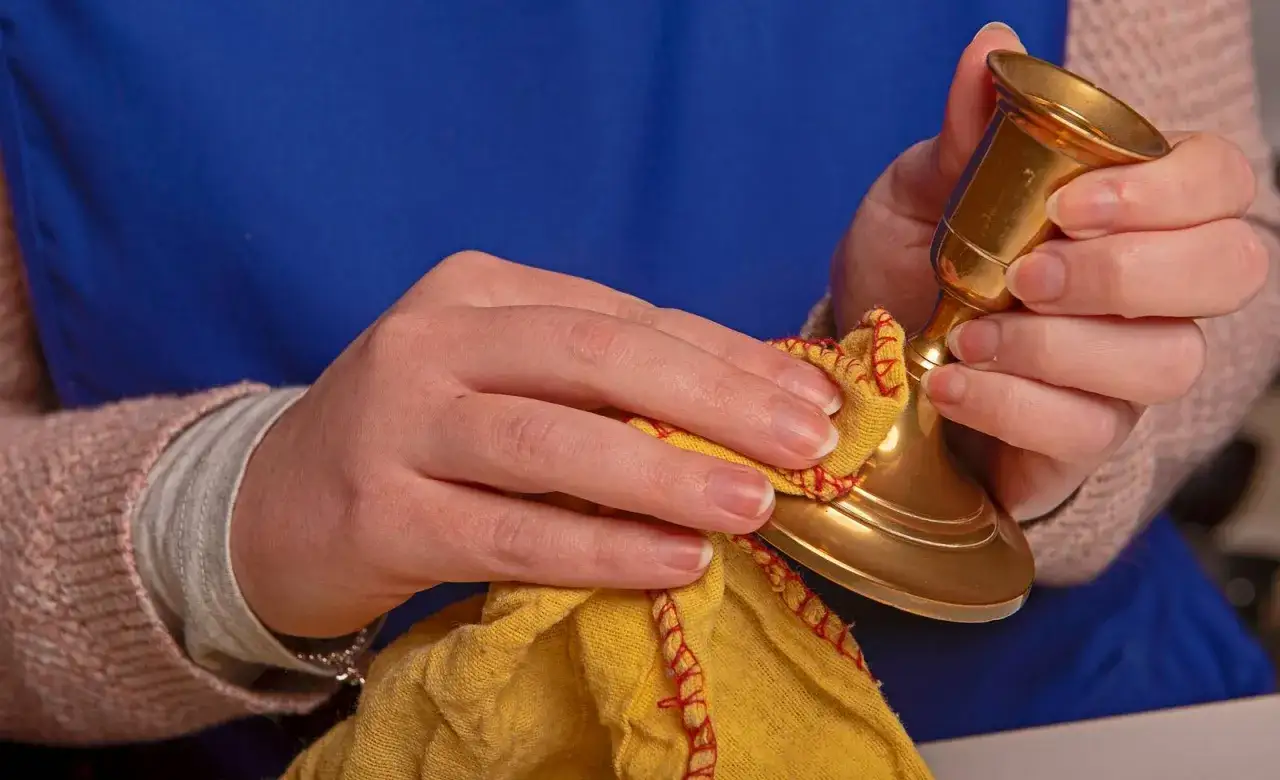 H&auml;nde polieren einen goldenen Kerzenst&auml;nder mit einem gelben Tuch. Messing reinigen f&uuml;r neuen Glanz.