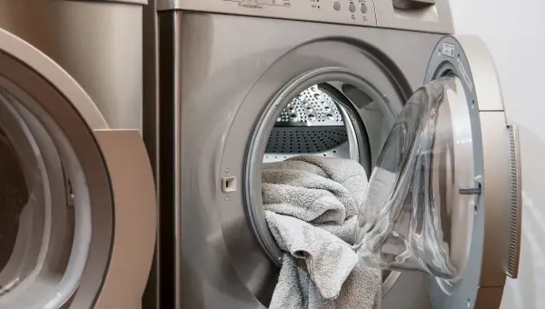 Waschmaschine mit offener Tür und grauen Handtüchern. Perfekt, um hartnäckige colaflecken entfernen zu lassen.