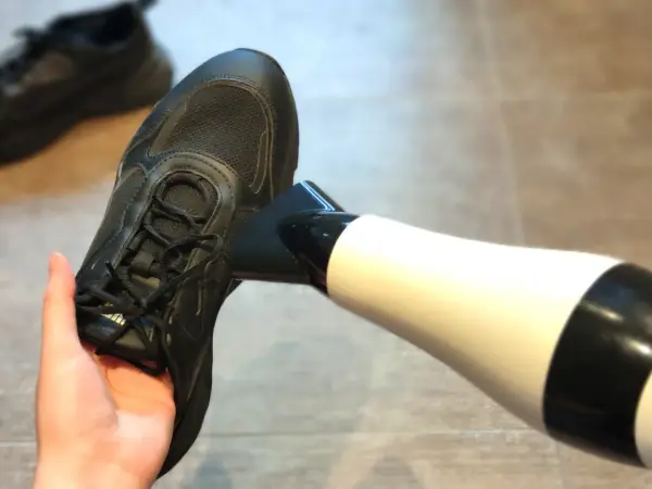 Schwarze Turnschuhe trocknen mit einem Föhn. Ein Paar nasse Schuhe wird mit einem Föhn getrocknet, um sie schnell wieder einsatzbereit zu machen.